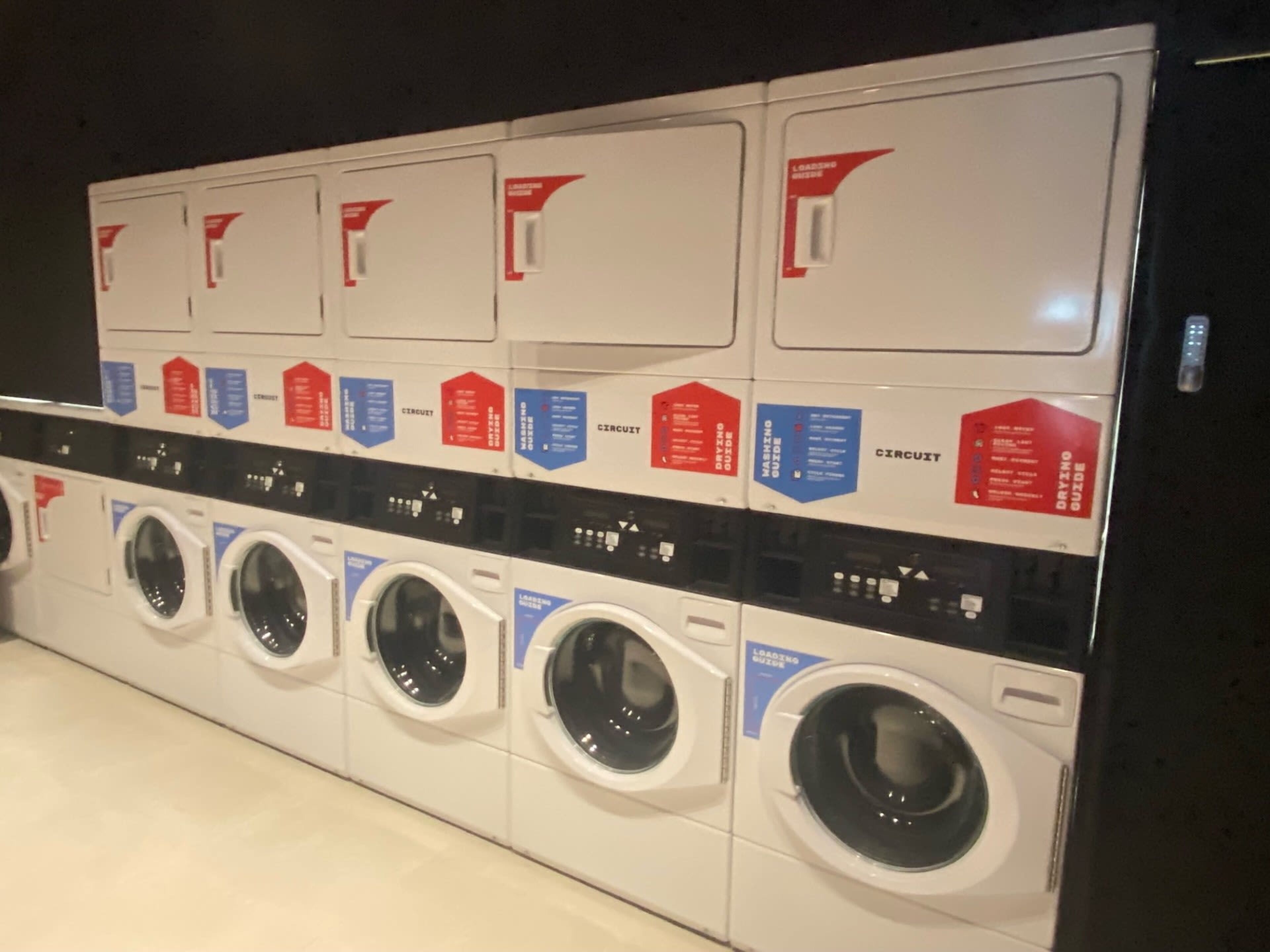 A row of white washing machines with control panels and instructional labels.