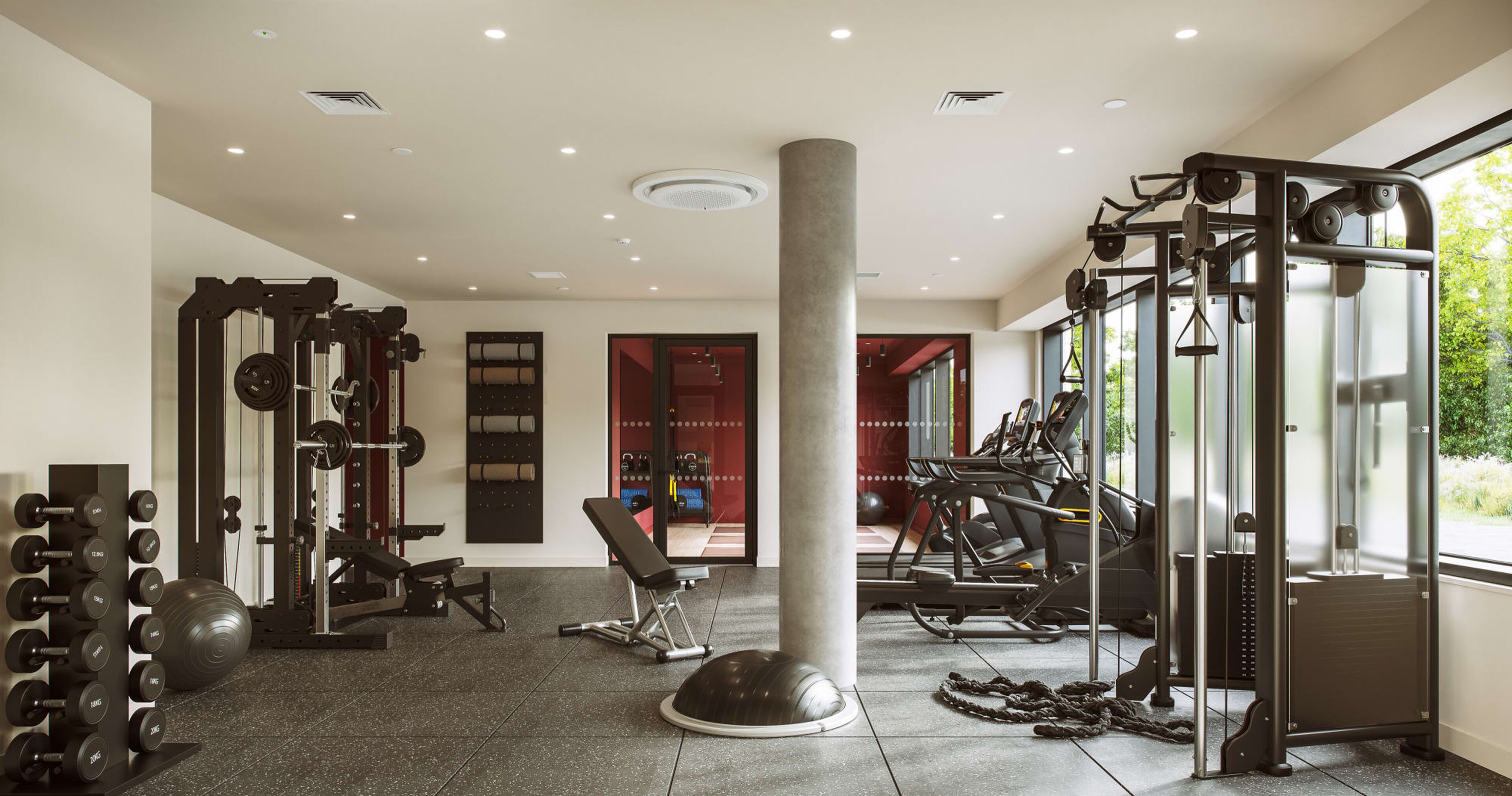 Ein Fitnessstudio mit verschiedenen Trainingsgeräten, einem Gewittergestell und einer großen Säule.