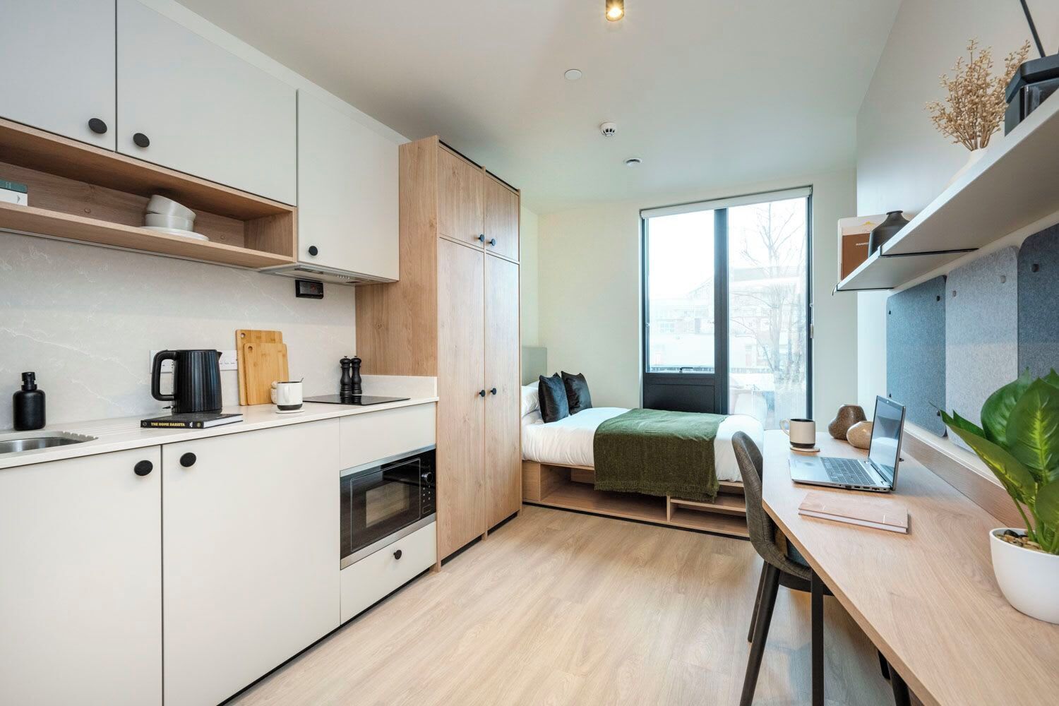 Une petite pièce comprenant un coin cuisine, un lit et un bureau avec un ordinateur portable.