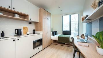 Une petite pièce comprenant un coin cuisine, un lit et un bureau avec un ordinateur portable.