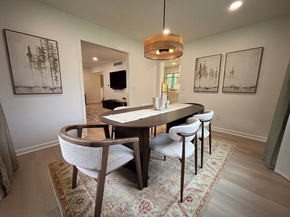 Un comedor con una mesa de madera, cuatro sillas, una lámpara colgante y obras de arte en las paredes.