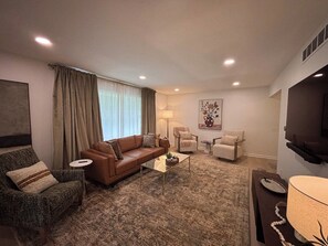 A living room with a brown sofa, two armchairs, a coffee table, and a flat-screen TV mounted on the wall. - Covenanter Classic | Luxe East Side Retreat (Bloomington)