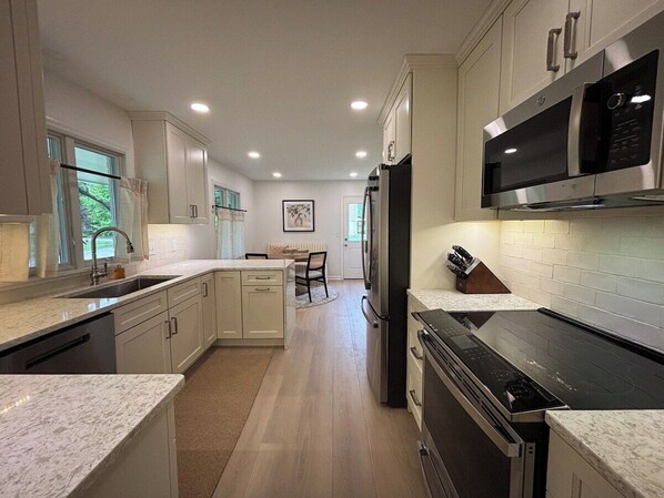 A modern kitchen with a central island, built-in appliances, and a dining area in the background. - Covenanter Classic | Luxe East Side Retreat (Bloomington)