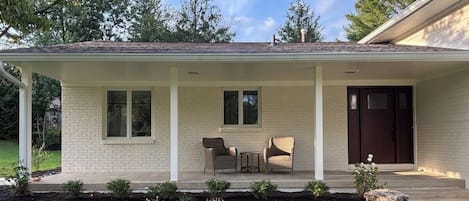 Ein eingeschossiges Haus mit einer Veranda, einer Haustür und zwei Fenstern.