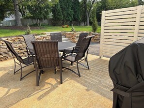Un patio al aire libre con un muro de piedra, una mesa redonda y cuatro sillas de mimbre.