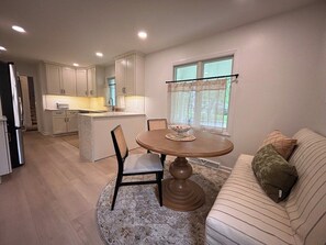 A modern kitchen with white cabinets, a dining table with chairs, and a sofa with cushions. - Covenanter Classic | Luxe East Side Retreat (Bloomington)