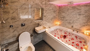 Un baño moderno con suelo de mármol, una bañera blanca con pétalos de rosa, un inodoro y una zona de ducha.