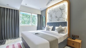 Un dormitorio moderno con una cama grande, un ventilador de techo, un cabecero con diseño de mármol, una mesita de noche con un teléfono y vistas a zonas verdes por la ventana.
