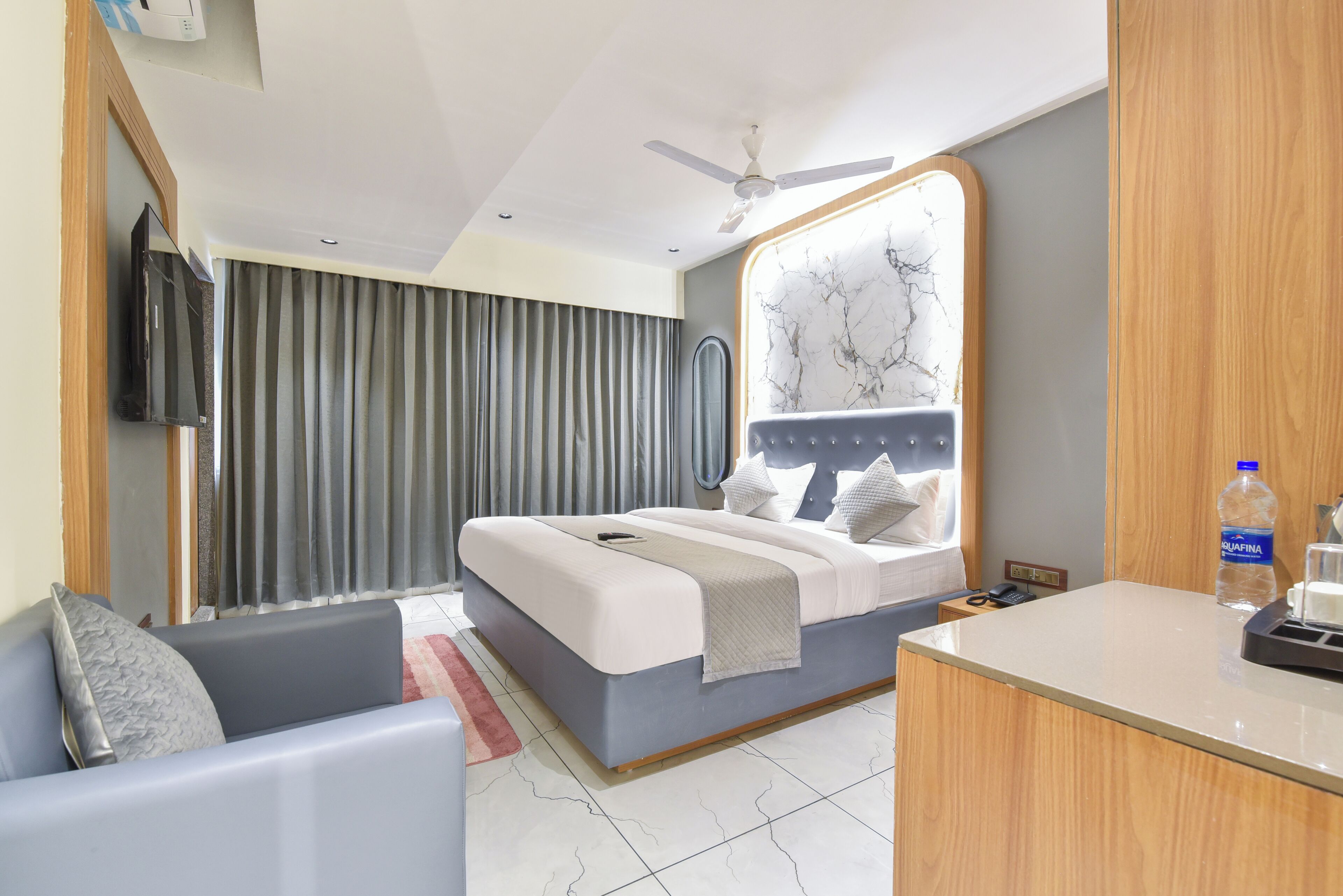 A hotel room with a bed, a desk, a chair, a TV, and a ceiling fan.