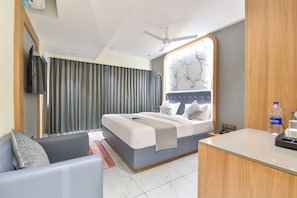Una habitación de hotel con una cama, un escritorio, una silla, un televisor y un ventilador de techo.
