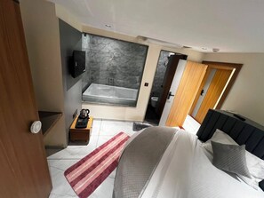 Un dormitorio moderno con una cama grande, televisor, baño con bañera y puerta de madera.