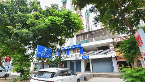 Un SUV blanco estacionado frente a un hotel llamado 'Prime Icon' con un letrero azul.