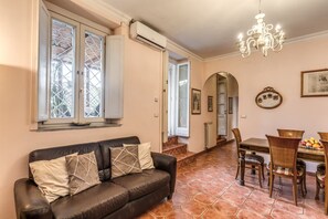 Ein Wohnzimmer mit einer Ledersofa, einem Esstisch mit Stühlen, einer Kandelaber und Blick durch die offene Tür.