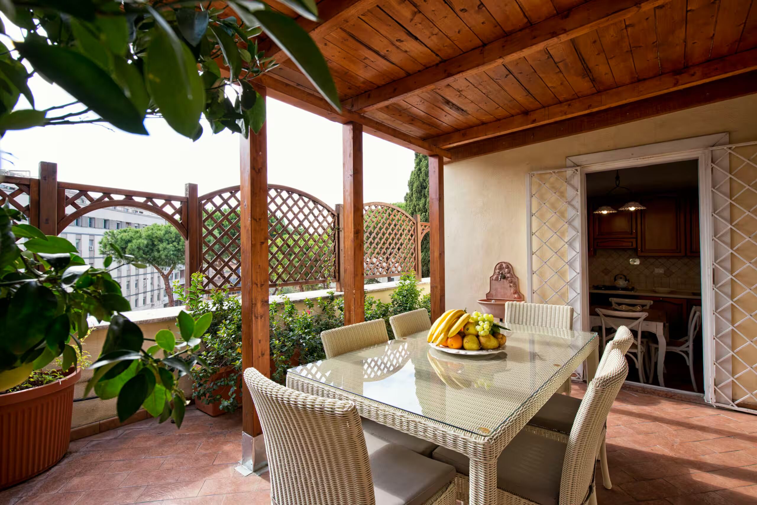 An outdoor patio with a table set for dining, surrounded by wicker chairs, and a view of the cityscape.