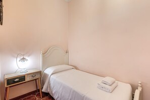 Een kleine kamer met een enkel bed, een houten nachtkastje, een lamp en een radiator.