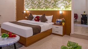 Un dormitorio moderno con una cama, mesitas de noche, un florero y un ventilador de techo, además de una pared decorada con un estampado de hojas tropicales y una planta en maceta.