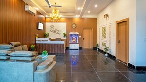 Zona de recepción de un hotel con mostrador, asientos, un candelabro y un cartel de recepción.
