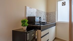 Una cocina compacta con un refrigerador negro, un microondas y un lavamanos. Hay una planta en maceta sobre la encimera.