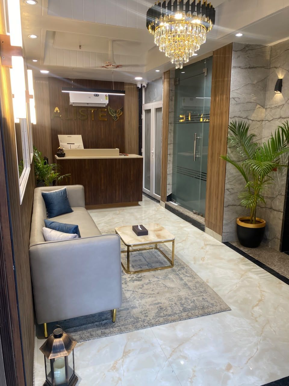 A modern lobby with a reception desk, seating area, and a chandelier.