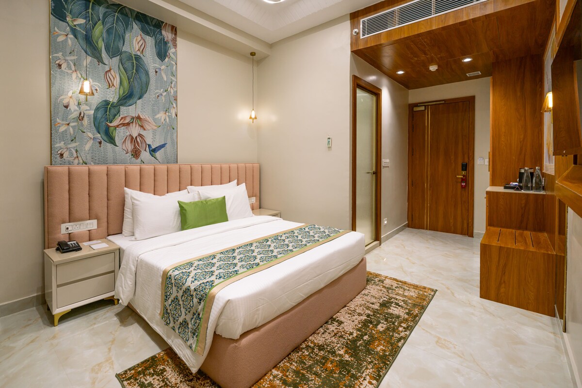 A hotel room with a large bed, a nightstand, a telephone, a wall-mounted light, a wooden wardrobe, and a door leading to another room.