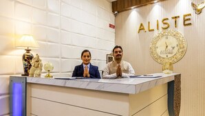 En receptionsdisk med to personer siddende, et ur og ordet 'ALISTE' på væggen.