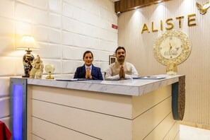Un mostrador de recepción con dos personas sentadas, un reloj y la palabra 'ALISTE' en la pared.