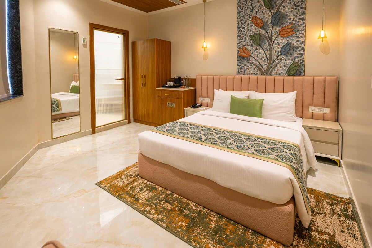 A hotel room with a large bed, a wooden wardrobe, a nightstand with a lamp, and a decorative wall piece.
