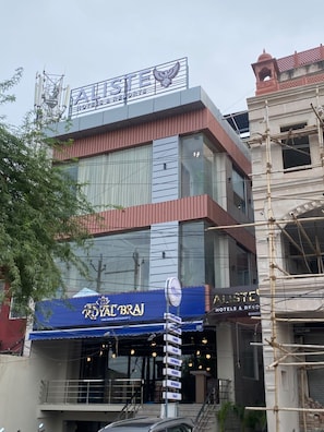 A hotel with a sign reading 'ALISTE HOTELS & RESORTS' and a blue awning with 'ROYAL BRAJ' written on it.