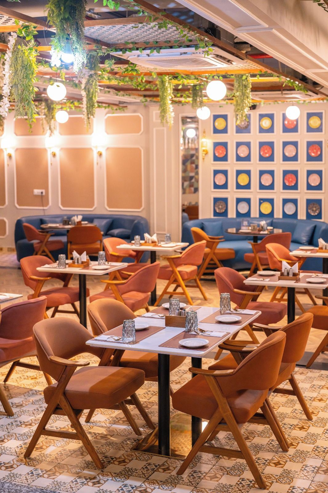 A restaurant interior with tables and chairs, hanging plants, and a wall with circular decorations.