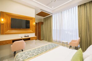 Een hotelkamer met een groot bed, een bureau met een flatscreen televisie, twee stoelen en een groot raam met gordijnen.