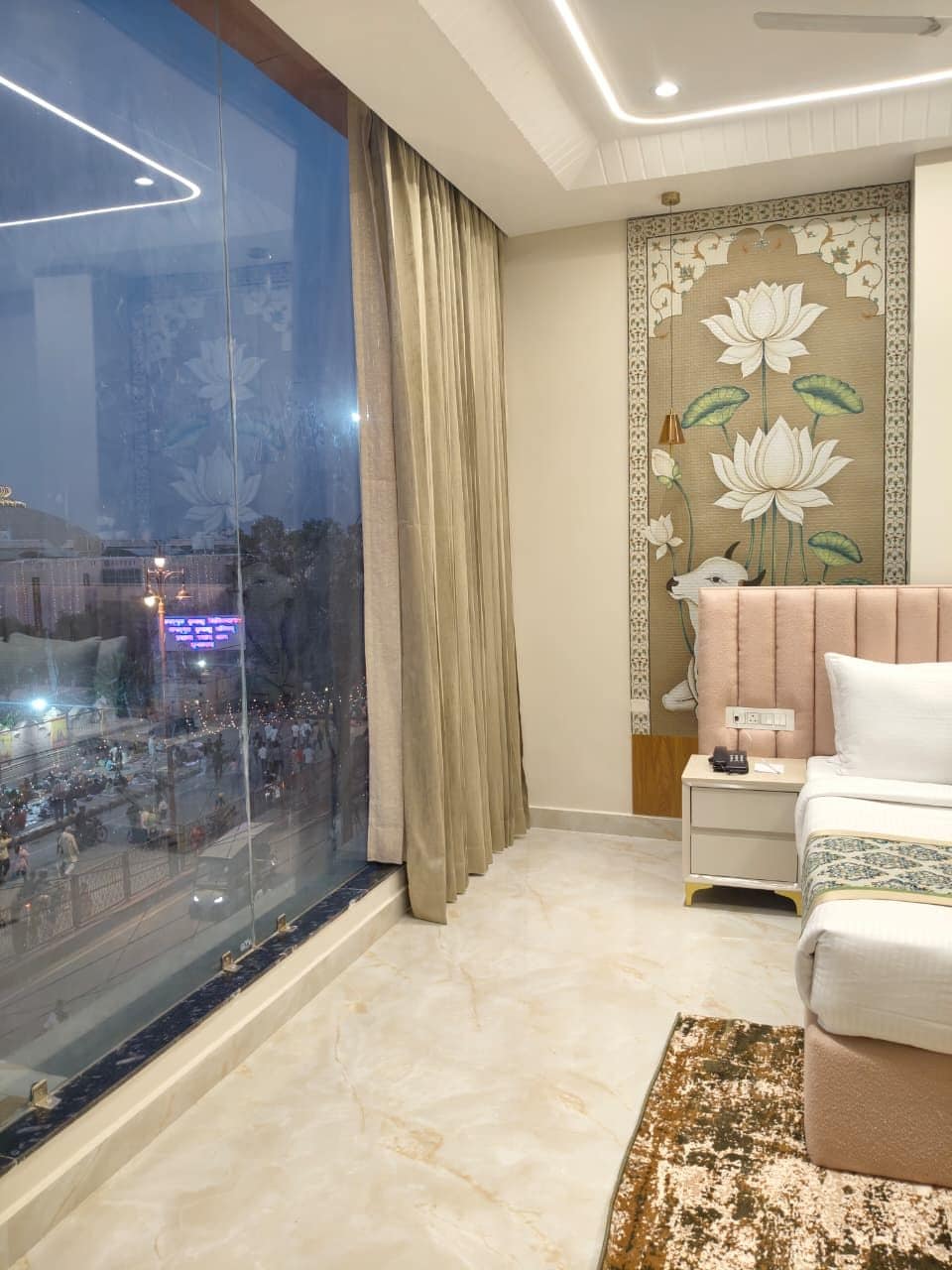 Habitación de hotel con un ventanal grande, una cama, una mesita de noche y un diseño decorativo de loto en la pared.