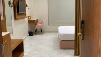 Un dormitorio moderno con una cama, un tocador con espejo, una silla rosa y un ventanal grande.