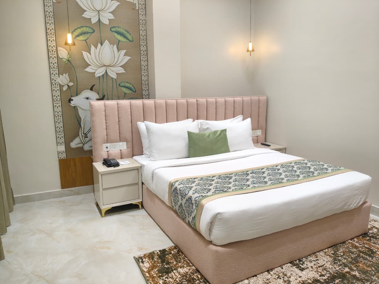 Una habitación de hotel con una cama, mesitas de noche, una lámpara de noche, una pared con un mural floral y una manta decorativa.