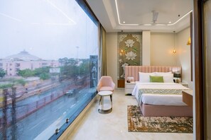 A hotel room with a large window, a bed, a bedside table, a chair, and a decorative wall panel.