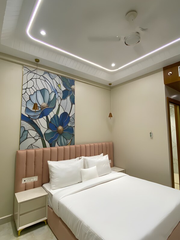 A modern bedroom with a large bed, a nightstand, a wall-mounted artwork, and recessed ceiling lighting.