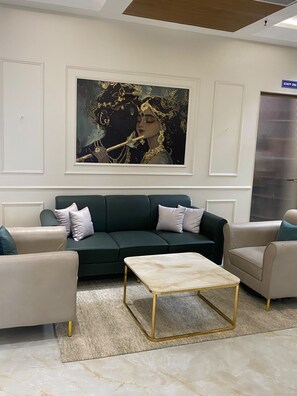 A living room with a dark green sofa, two armchairs, a marble coffee table, and a large framed artwork on the wall.