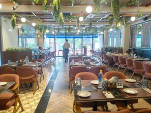 A spacious restaurant with multiple dining tables and chairs, a patterned floor, and hanging plants.