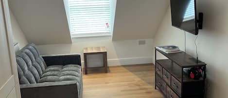 A loft bedroom with a sloped ceiling, a sofa, a TV, a desk, and a small table.