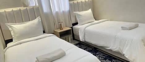 Une chambre d’hôtel avec deux lits, chacun doté de draps et d’oreillers blancs, une table de chevet avec une lampe et un tapis à motifs sombres.