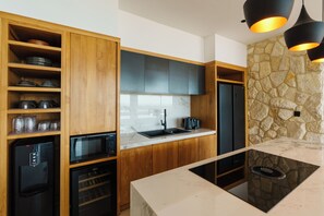 A modern kitchen with wooden cabinets, a stone accent wall, and a black refrigerator. - Villa Solaia by Alfred in Bali (Pecatu)