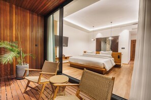 A modern hotel room with a large bed, a sitting area with chairs, a potted plant, and a view through a glass door. - Villa Solaia by Alfred in Bali (Pecatu)