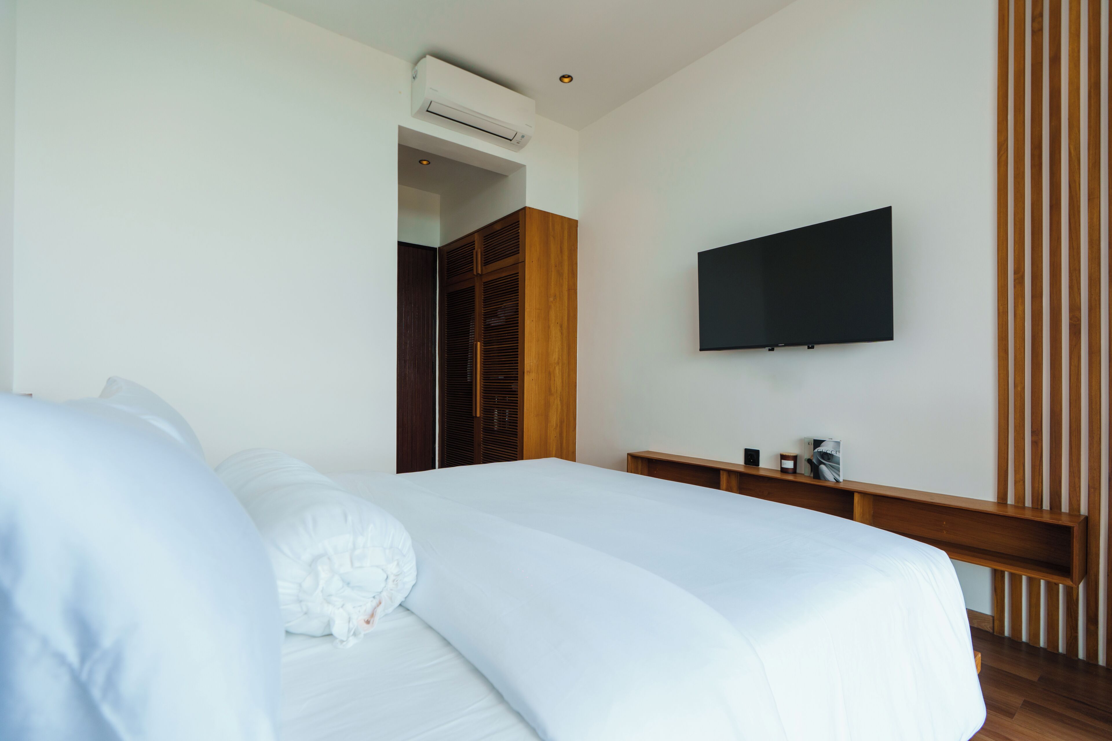 A hotel room with a large bed, a flat-screen TV mounted on the wall, and a wooden wardrobe.