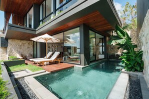 A modern house with a swimming pool, lounge chairs, and a wooden deck. - Villa Solaia by Alfred in Bali (Pecatu)