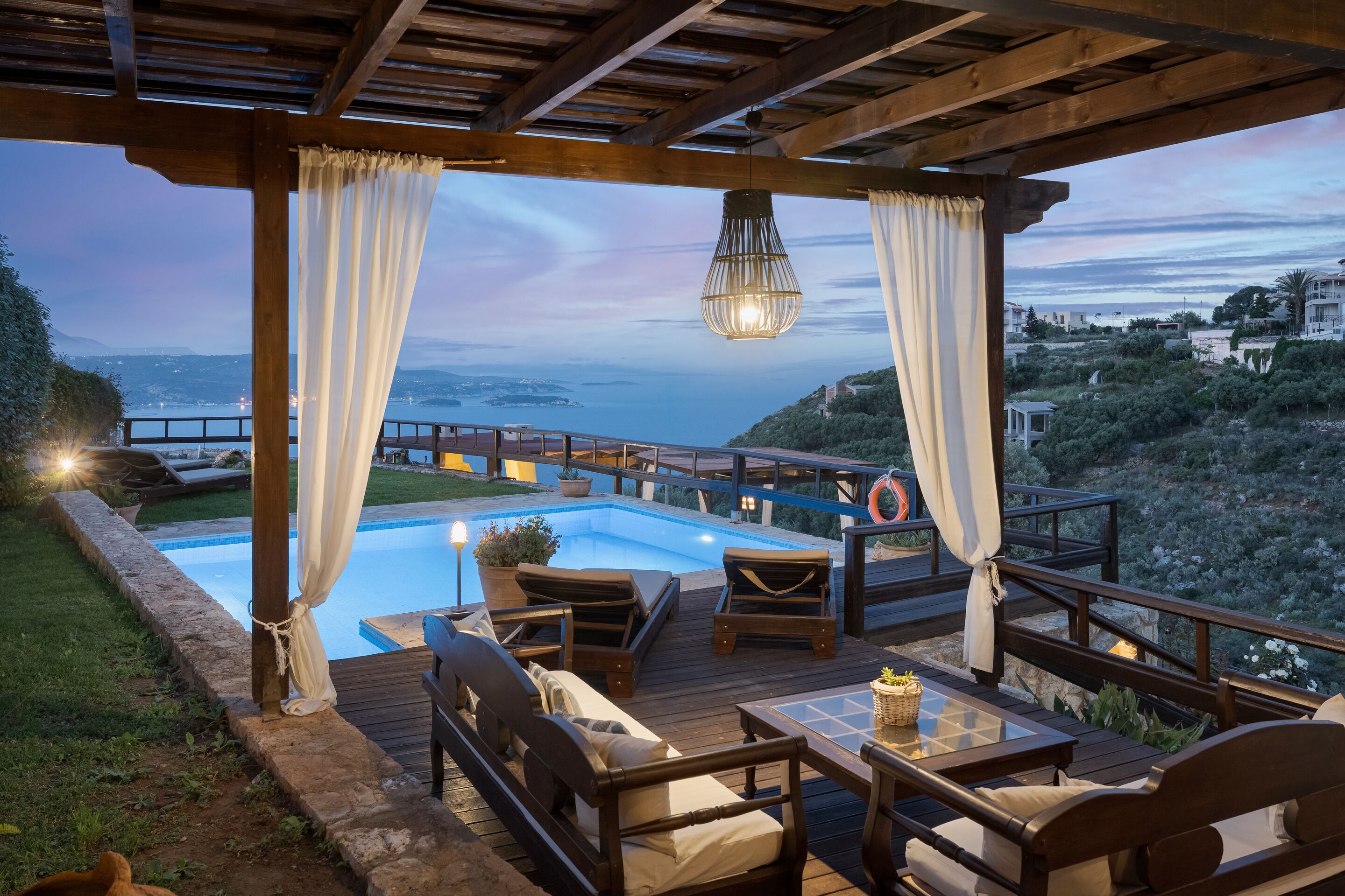 A poolside area with a view of the sea, wooden deck, lounge chairs, and a table.