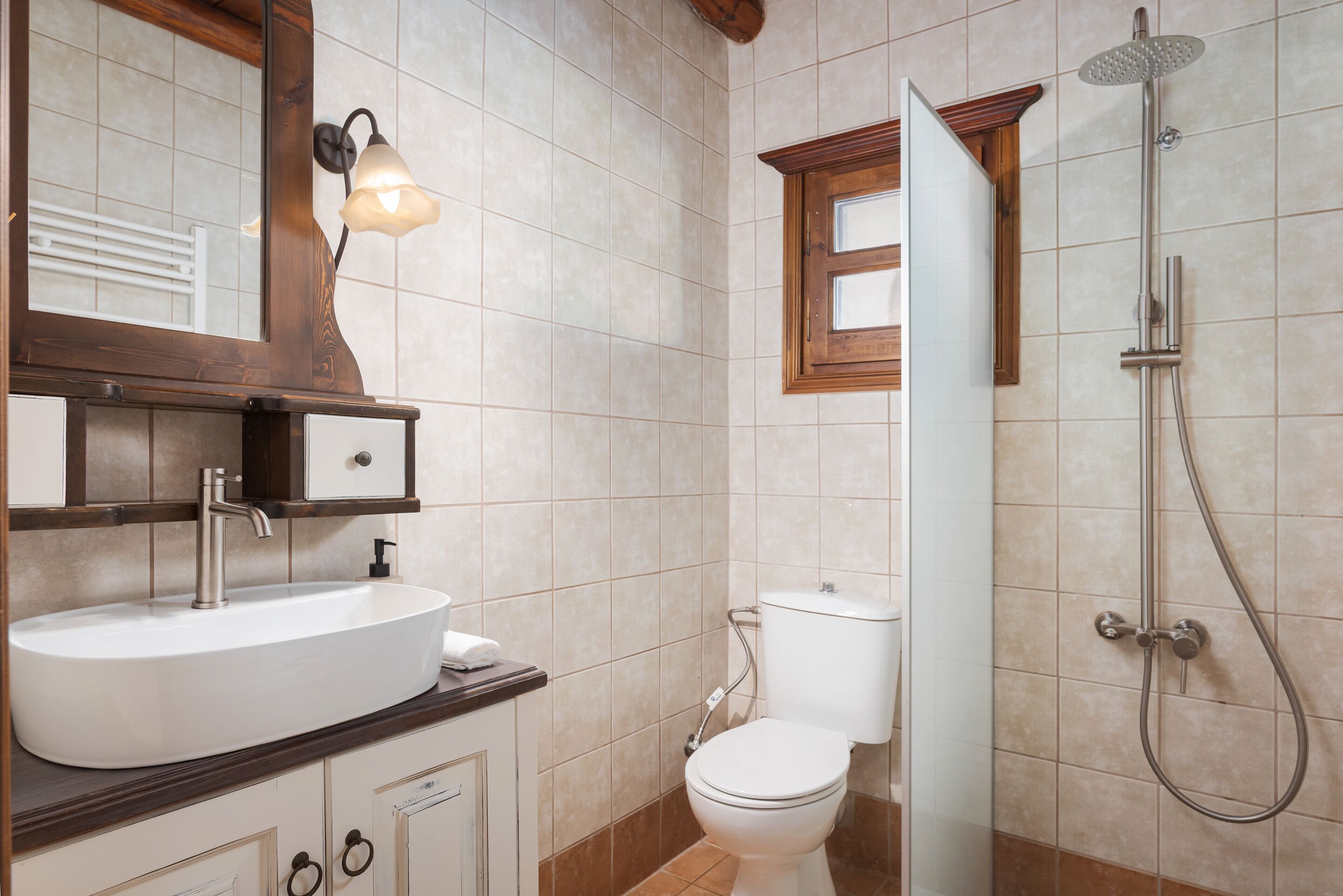 A bathroom with a sink, mirror, toilet, shower, and a window.