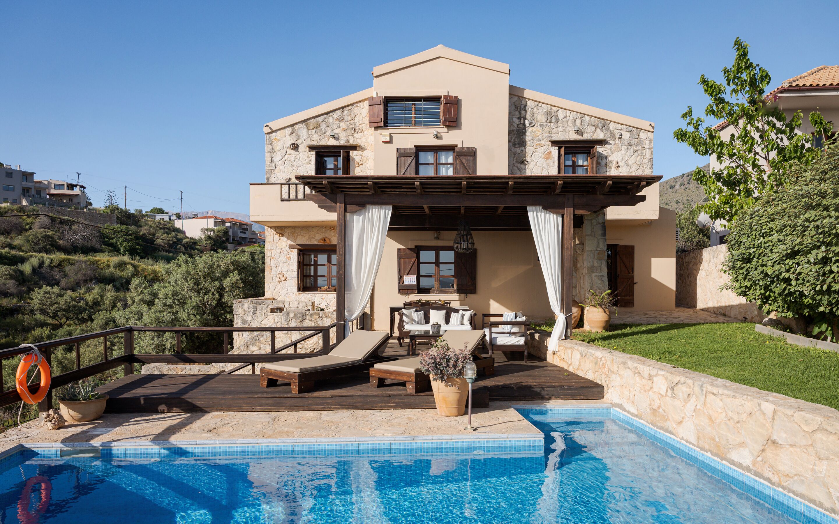 A two-story building with a pool, outdoor furniture, and a stone facade.
