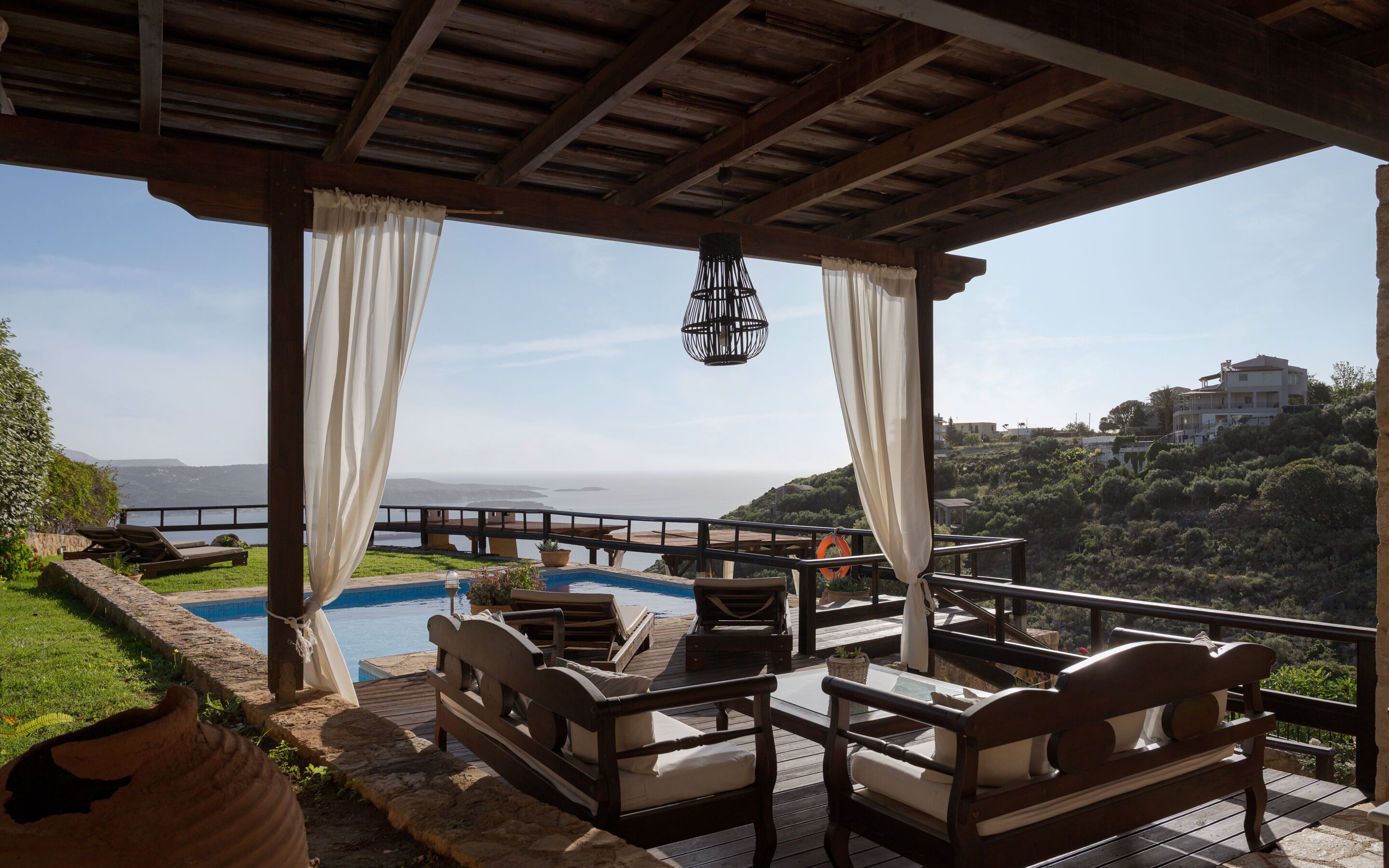 Ein überdachter Außenbereich mit Pool, Liegestühlen und Meerblick.