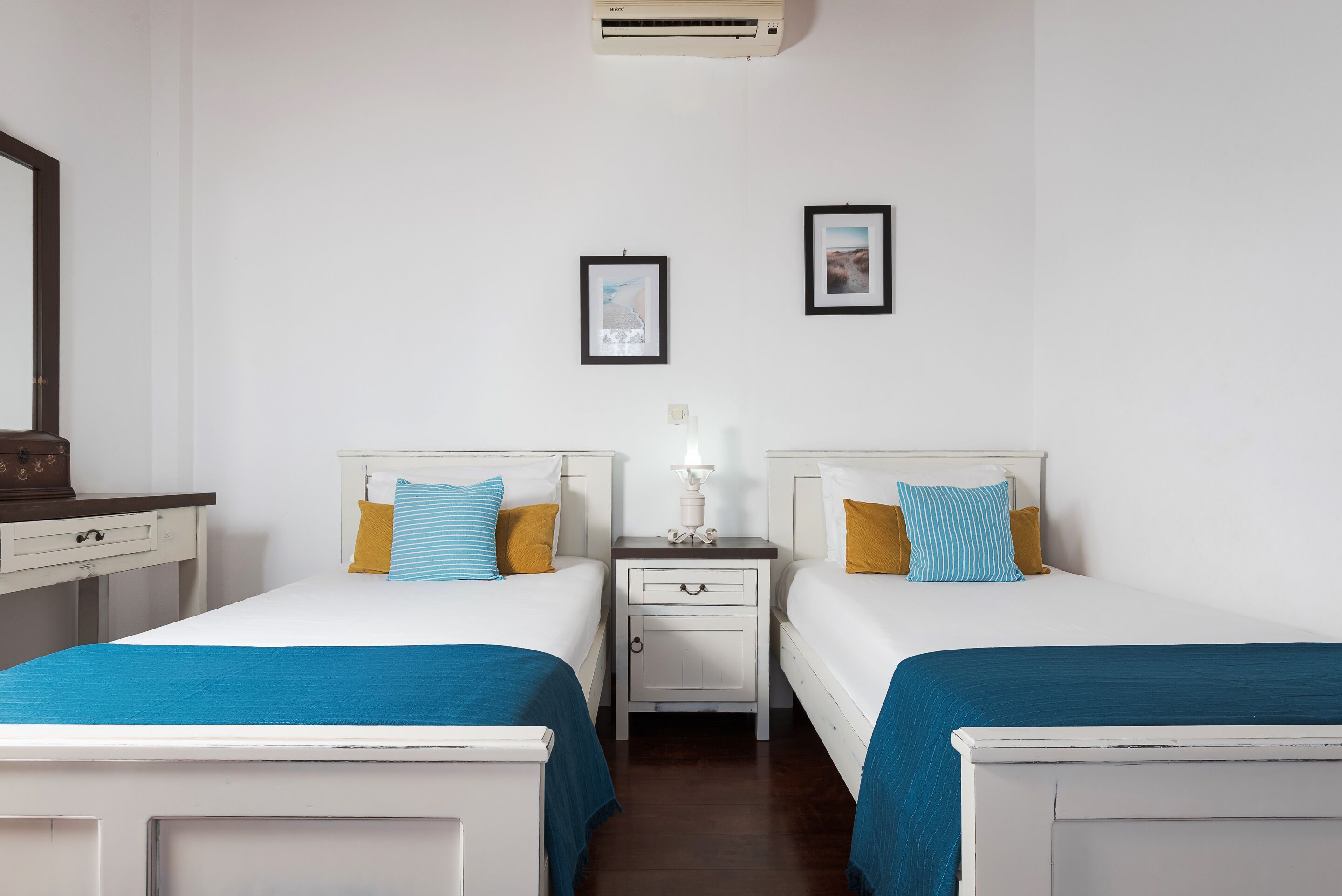 Een tweepersoonskamer met twee bedden, een nachtkastje met een lamp en een wandairconditioner.