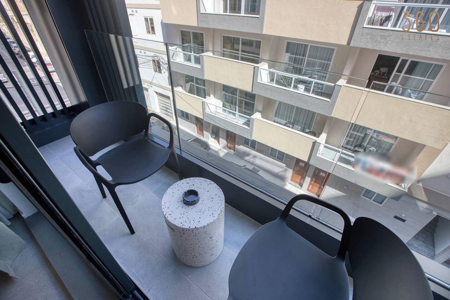 Un balcone con due sedie e un tavolino, affaccia su un edificio a più piani con balconi.