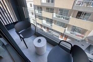 Un balcone con due sedie e un tavolino, affaccia su un edificio a più piani con balconi.